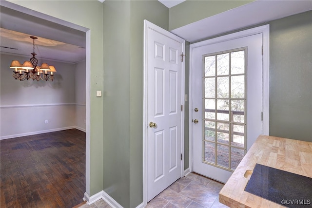 doorway to outside featuring visible vents, a notable chandelier, baseboards, and wood finished floors