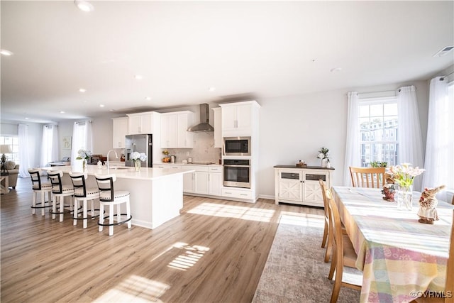 kitchen with a center island with sink, white cabinets, wall chimney exhaust hood, appliances with stainless steel finishes, and light countertops