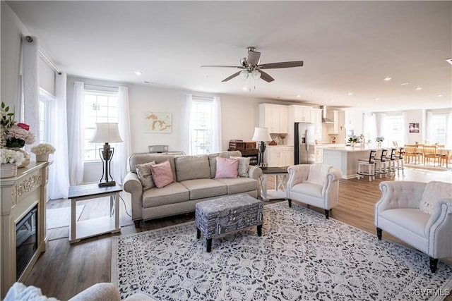 living room featuring a ceiling fan, a glass covered fireplace, light wood-style flooring, and recessed lighting