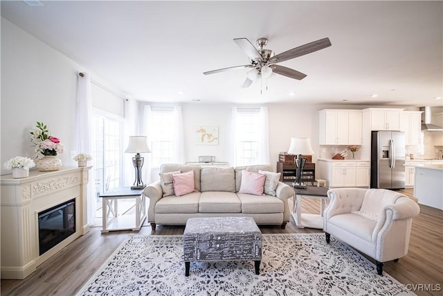 living area featuring ceiling fan, a glass covered fireplace, wood finished floors, and recessed lighting