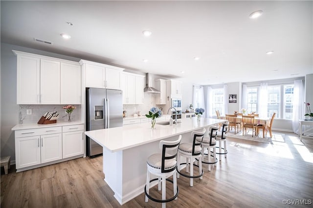 kitchen featuring wall chimney exhaust hood, a center island with sink, and white cabinets