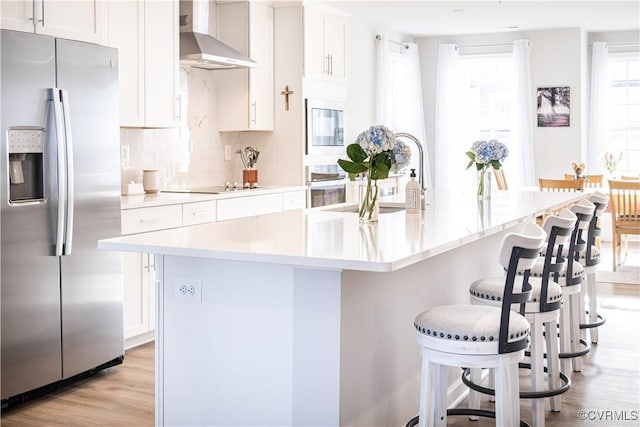 kitchen with black appliances, a center island with sink, light countertops, and wall chimney range hood