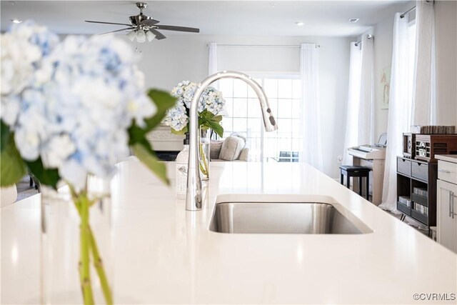 kitchen with ceiling fan, light countertops, a sink, and white cabinetry