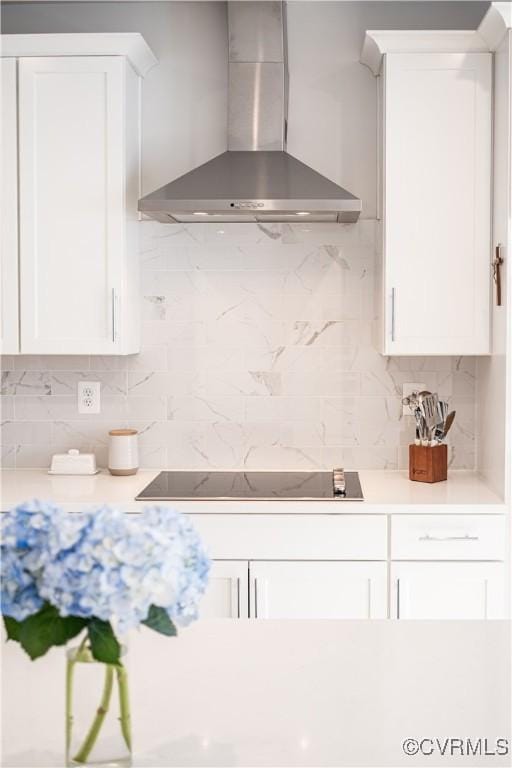 kitchen with decorative backsplash, white cabinets, black electric cooktop, light countertops, and wall chimney range hood