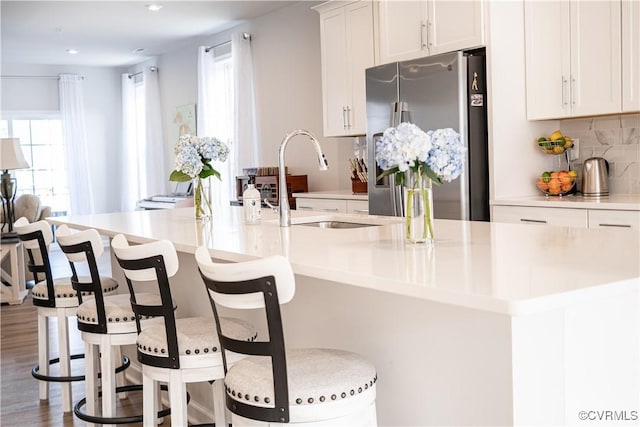 kitchen featuring light countertops, stainless steel refrigerator with ice dispenser, a large island with sink, and white cabinets