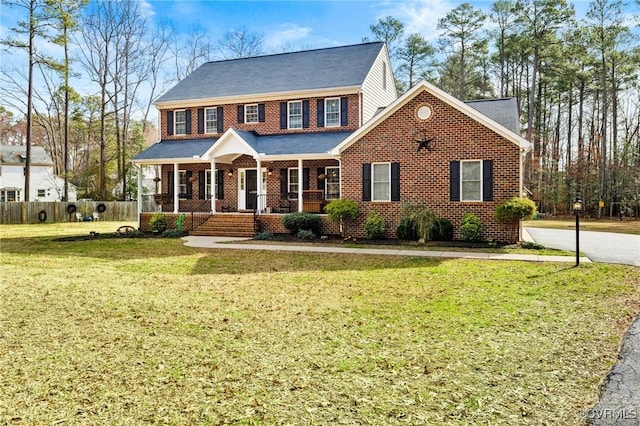 view of front of house featuring brick siding, covered porch, a front yard, and fence