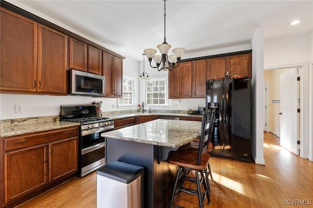 kitchen featuring light wood-type flooring, a breakfast bar, light stone counters, a center island, and stainless steel appliances