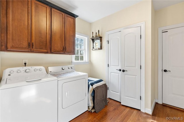 clothes washing area with washer and dryer, cabinet space, and wood finished floors