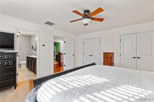 bedroom with baseboards, visible vents, ensuite bath, ceiling fan, and two closets