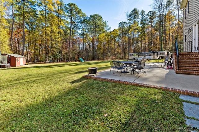 view of yard featuring an outbuilding, a patio, a shed, a playground, and a view of trees