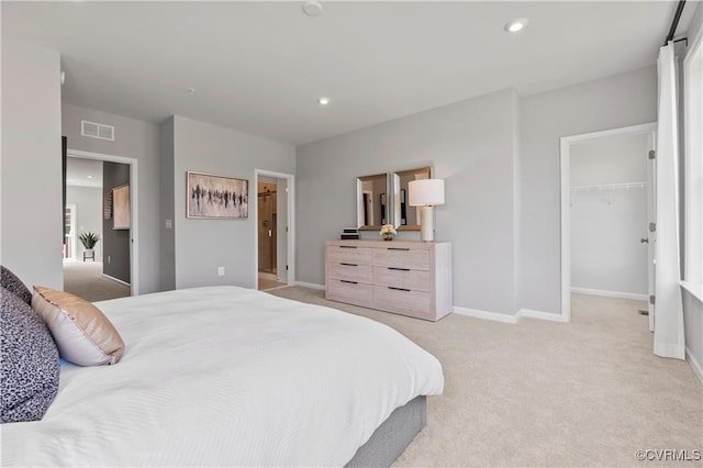 bedroom with a walk in closet, recessed lighting, light colored carpet, visible vents, and baseboards