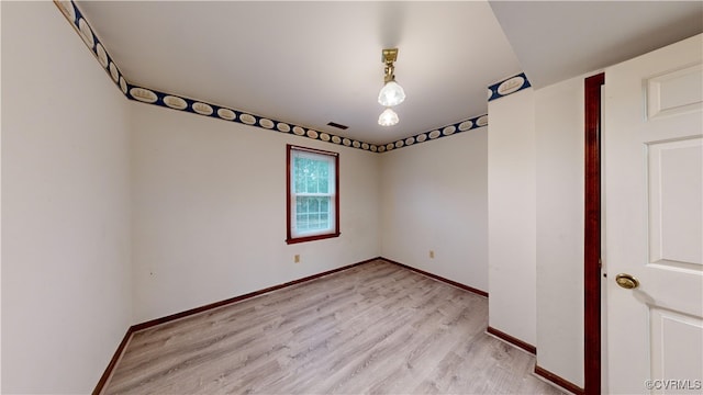 spare room featuring light wood finished floors, visible vents, and baseboards