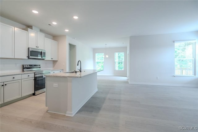 kitchen featuring tasteful backsplash, a center island with sink, white cabinets, stainless steel appliances, and a sink