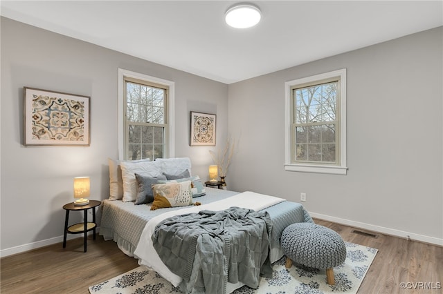 bedroom with multiple windows, baseboards, and wood finished floors