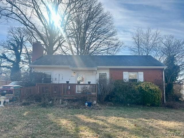 rear view of property featuring a yard, a chimney, brick siding, and a wooden deck