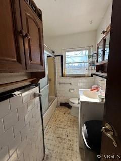 bathroom featuring tile walls, combined bath / shower with glass door, vanity, and toilet