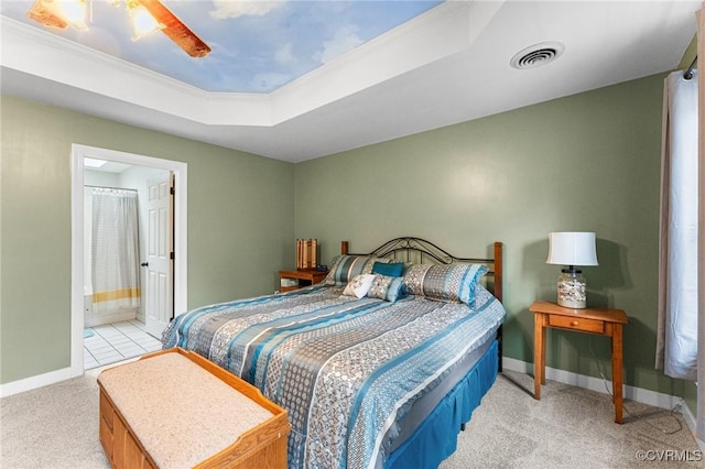 bedroom featuring baseboards, visible vents, ensuite bath, light carpet, and a raised ceiling