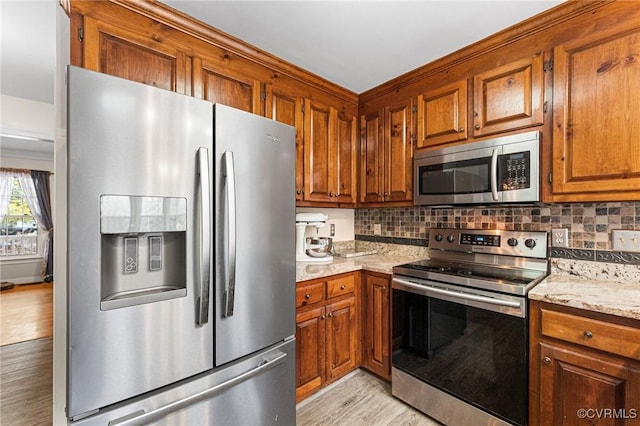 kitchen with stainless steel appliances, brown cabinets, light wood-style floors, and decorative backsplash