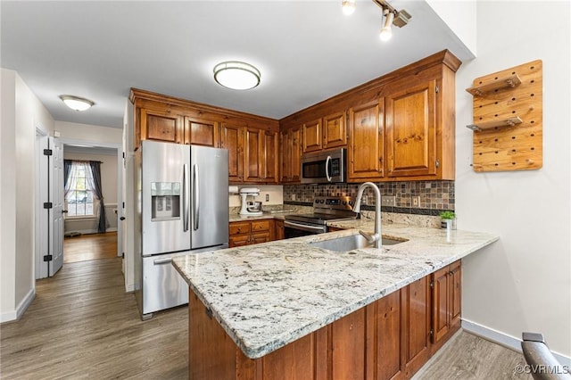 kitchen with a sink, tasteful backsplash, appliances with stainless steel finishes, a peninsula, and brown cabinetry