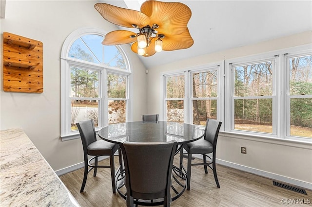 dining space featuring a ceiling fan, wood finished floors, visible vents, baseboards, and lofted ceiling