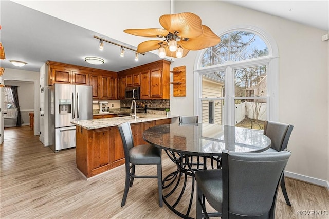 kitchen with a peninsula, light wood-style flooring, stainless steel appliances, brown cabinets, and backsplash