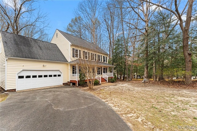 colonial home with an attached garage, covered porch, driveway, and roof with shingles