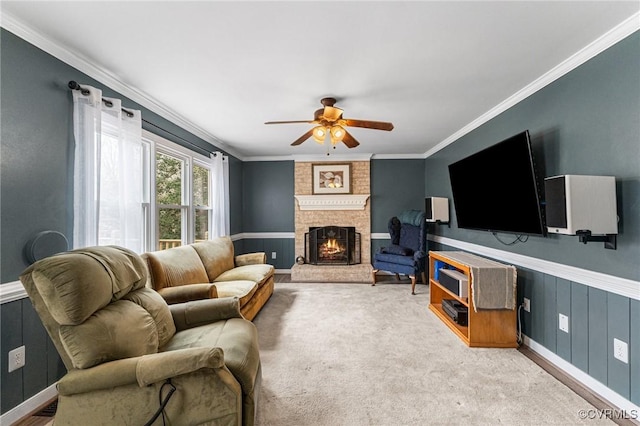 carpeted living room with a wainscoted wall, a brick fireplace, ornamental molding, and a ceiling fan