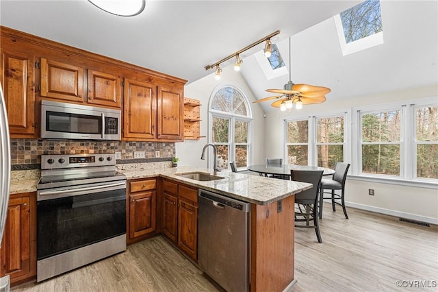 kitchen with decorative backsplash, vaulted ceiling with skylight, a peninsula, stainless steel appliances, and a sink