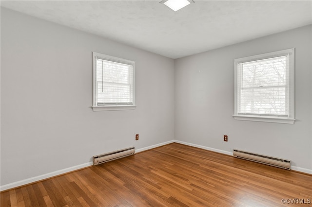 unfurnished room featuring wood finished floors, a wealth of natural light, and a baseboard radiator