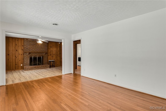 unfurnished living room with visible vents, wood walls, a fireplace, wood finished floors, and a textured ceiling