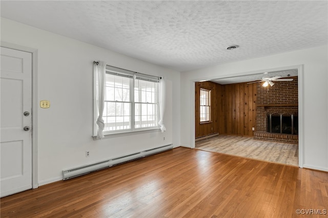 unfurnished living room featuring visible vents, a baseboard heating unit, a textured ceiling, wood finished floors, and a fireplace