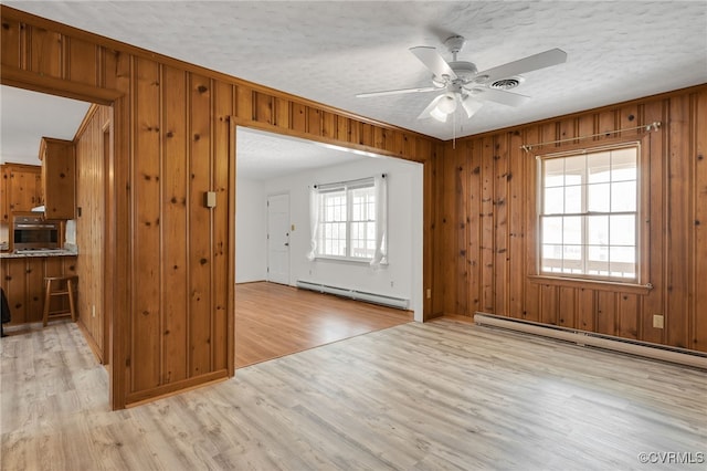 interior space featuring wooden walls, a baseboard radiator, light wood-style flooring, a textured ceiling, and a baseboard heating unit