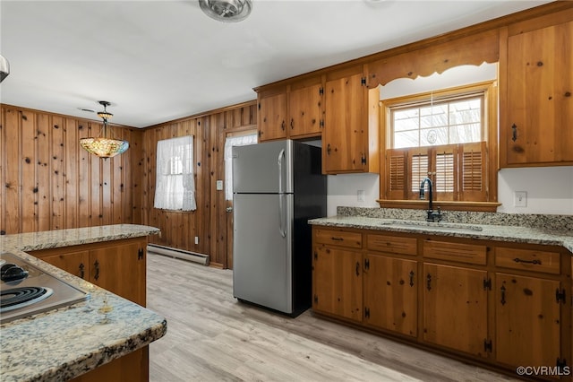 kitchen featuring wooden walls, baseboard heating, brown cabinets, stainless steel appliances, and a sink