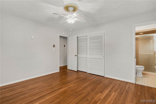 unfurnished bedroom with baseboards, wood finished floors, a closet, ensuite bath, and a ceiling fan