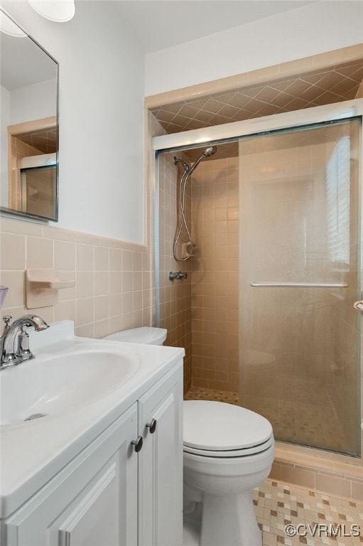 full bath featuring toilet, vanity, wainscoting, a stall shower, and tile walls