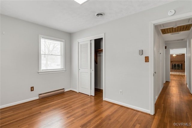 unfurnished bedroom with hardwood / wood-style floors, baseboards, visible vents, a closet, and a baseboard heating unit