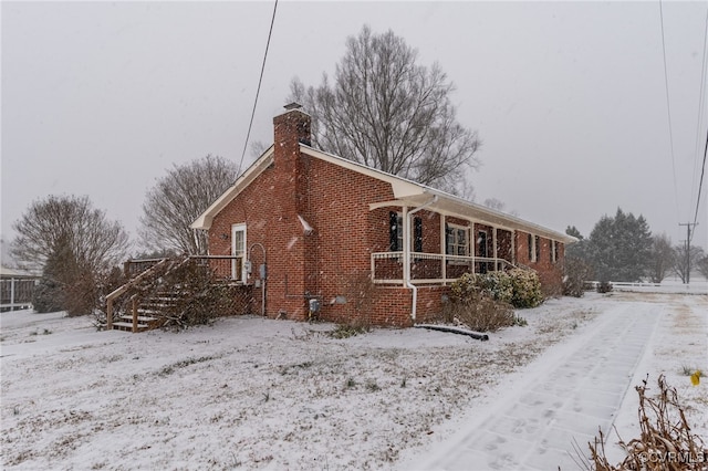 snow covered property with brick siding and a chimney