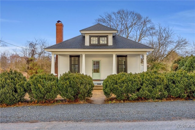 bungalow-style home with covered porch, roof with shingles, and a chimney