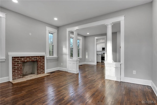 unfurnished living room with baseboards, dark wood-type flooring, a fireplace, and ornate columns