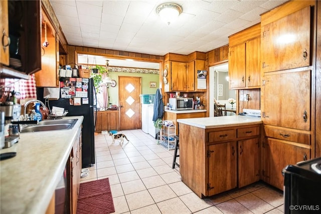 kitchen featuring brown cabinets, light countertops, stainless steel microwave, light tile patterned flooring, and a sink