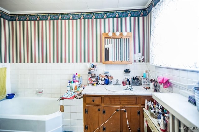 full bathroom featuring wallpapered walls, tile walls, ornamental molding, vanity, and a bath