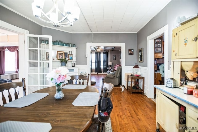 dining area with wood finished floors, wainscoting, crown molding, and an inviting chandelier