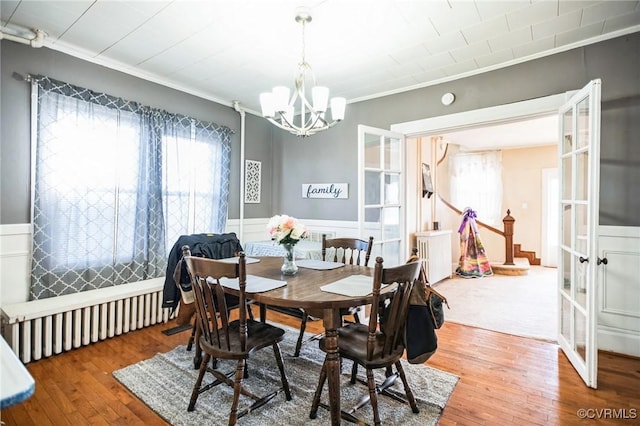 dining space with wood finished floors, ornamental molding, wainscoting, plenty of natural light, and an inviting chandelier