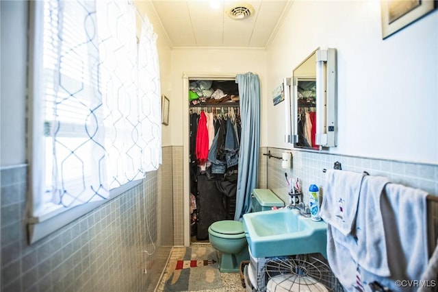 bathroom featuring a wainscoted wall, tile walls, visible vents, a spacious closet, and a sink