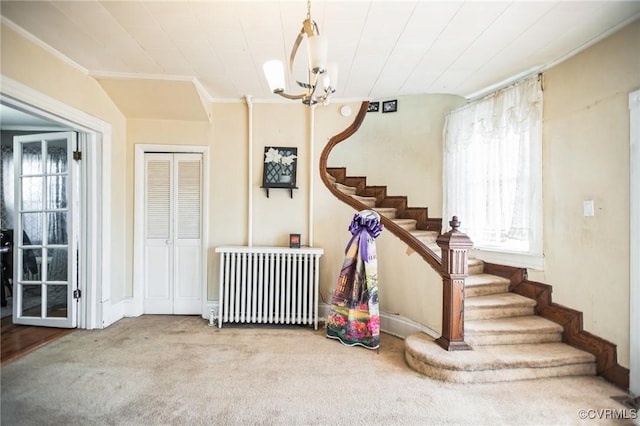 carpeted entrance foyer with stairs, radiator heating unit, a chandelier, and crown molding