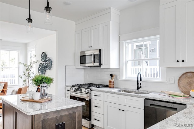 kitchen featuring appliances with stainless steel finishes, hanging light fixtures, light stone countertops, white cabinetry, and a sink