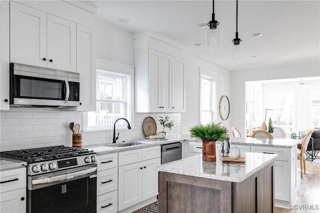 kitchen featuring white cabinets, appliances with stainless steel finishes, a center island, pendant lighting, and a sink