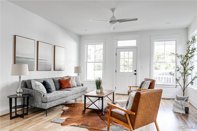 living area featuring baseboards, ceiling fan, and light wood finished floors