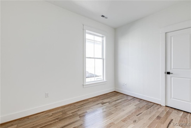 empty room with light wood finished floors, visible vents, and baseboards