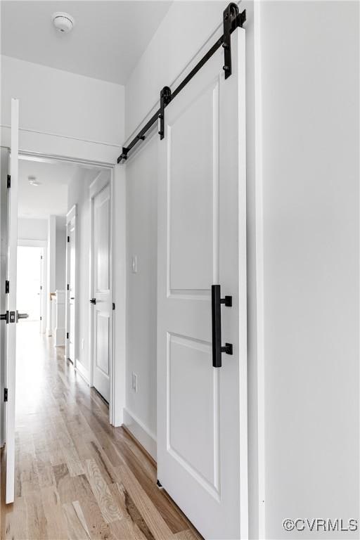 corridor featuring light wood-style floors, baseboards, and a barn door